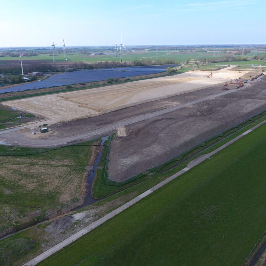 Bauarbeiten auf einem großen Grundstück mit Windkraftanlagen im Hintergrund.