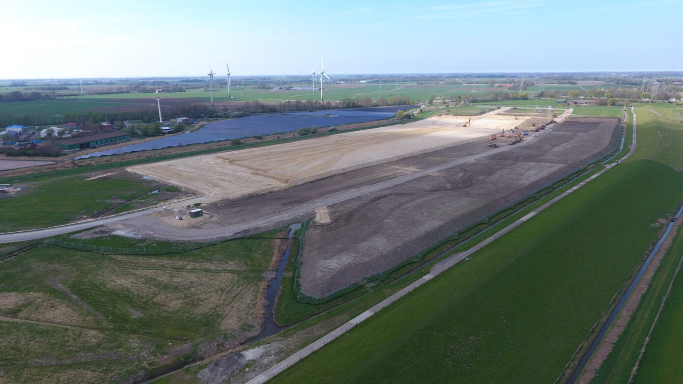 Bauarbeiten auf einem großen Grundstück mit Windkraftanlagen im Hintergrund.