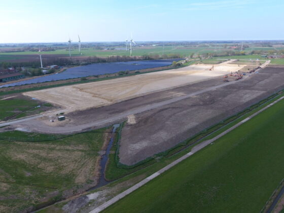 Bauarbeiten auf einem großen Grundstück mit Windkraftanlagen im Hintergrund.