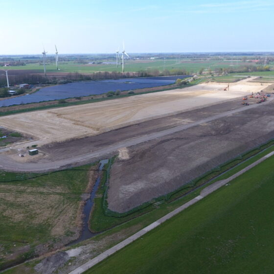 Bauarbeiten auf einem großen Grundstück mit Windkraftanlagen im Hintergrund.