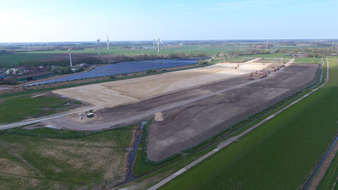 Bauarbeiten auf einem großen Grundstück mit Windkraftanlagen im Hintergrund.