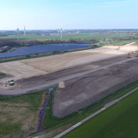 Bauarbeiten auf einem großen Grundstück mit Windkraftanlagen im Hintergrund.