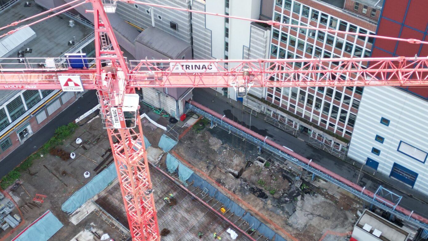 Baukran über Baustelle in städtischer Umgebung mit Bauarbeitern und Baustellenmaterial.
