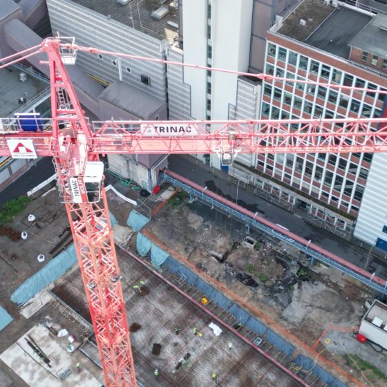 Baukran über Baustelle in städtischer Umgebung mit Bauarbeitern und Baustellenmaterial.