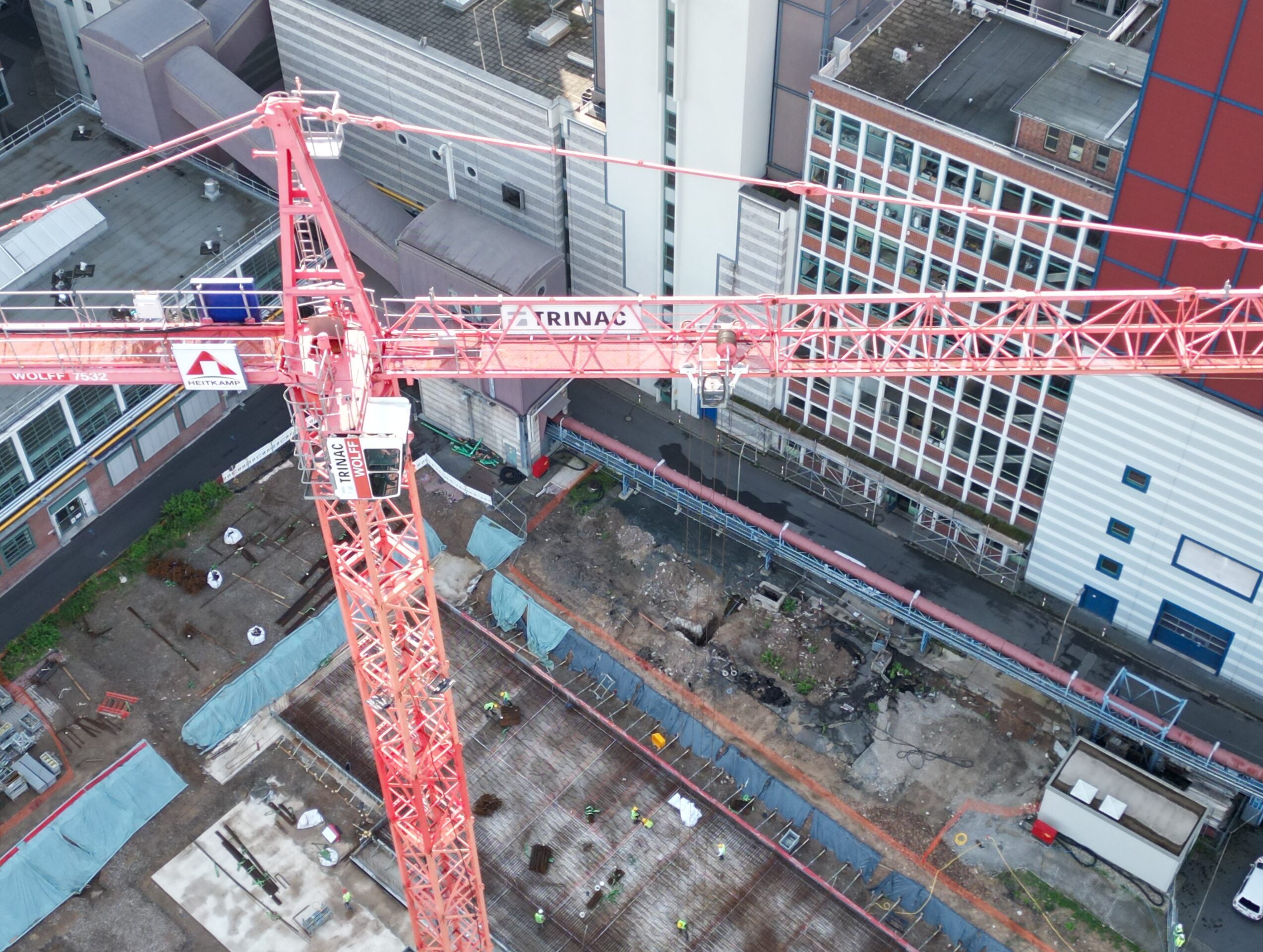 Baukran über Baustelle in städtischer Umgebung mit Bauarbeitern und Baustellenmaterial.