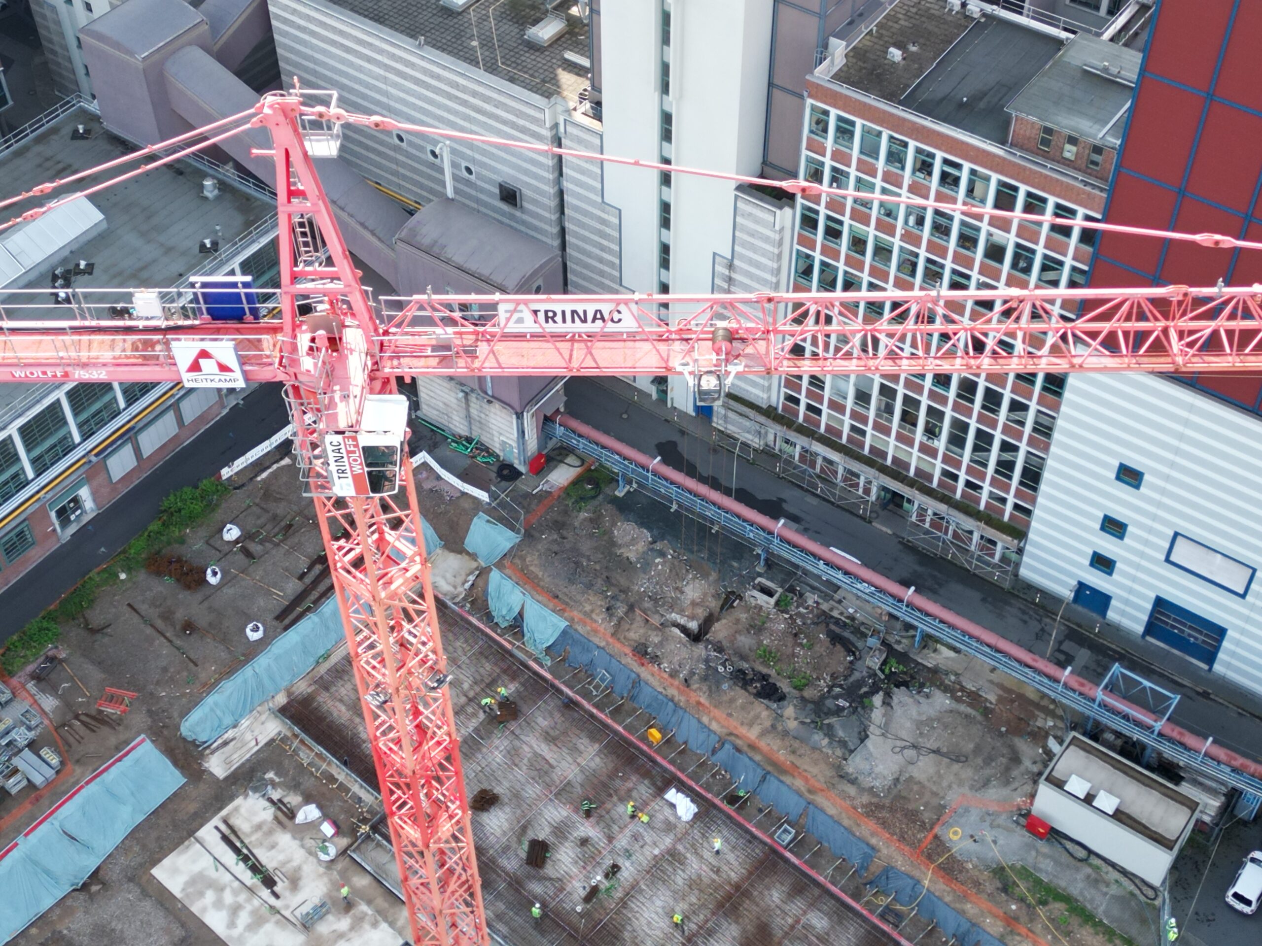 Baukran über Baustelle in städtischer Umgebung mit Bauarbeitern und Baustellenmaterial.