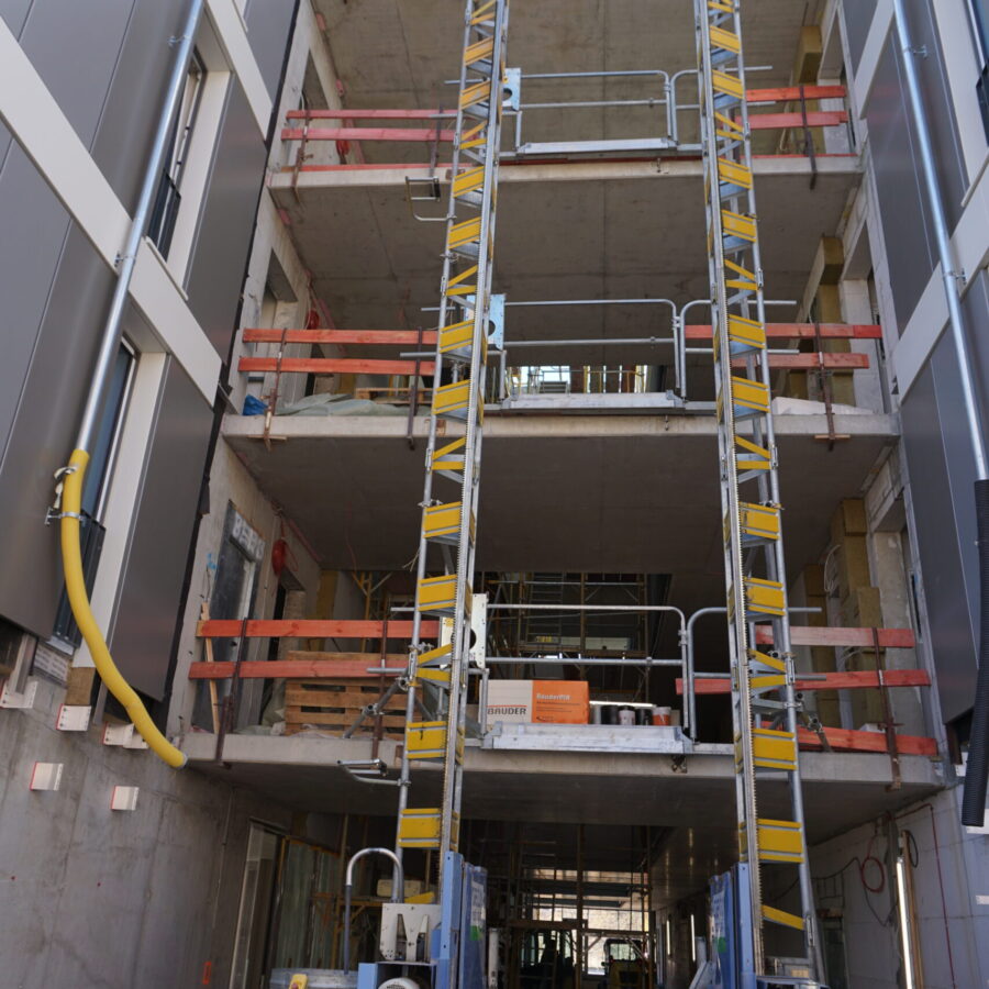 Baugerüst eines mehrstöckigen Gebäudes mit Aufzügen und Baustellenmaterialien.