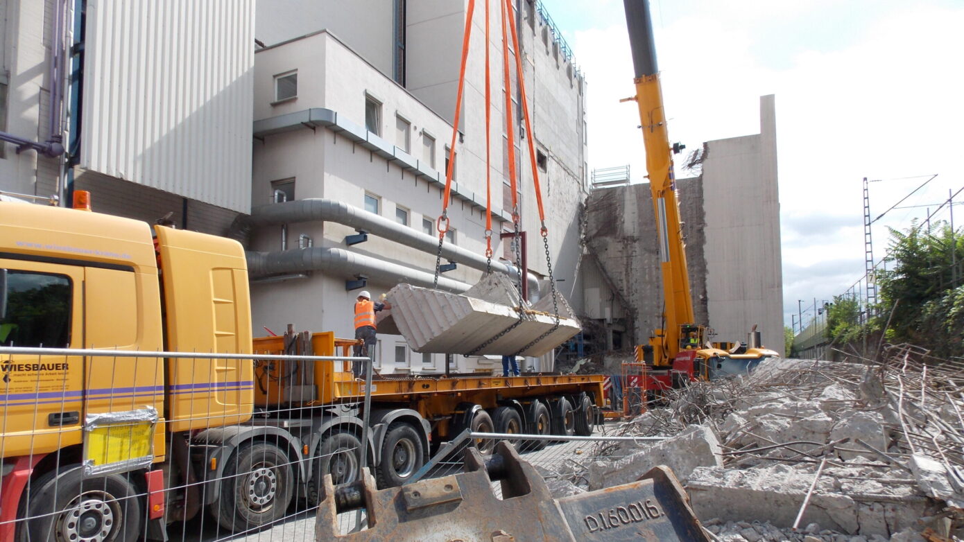 Bauarbeiten: Kranaushebung von Betonteilen auf einer Baustelle mit Abbrucharbeiten.