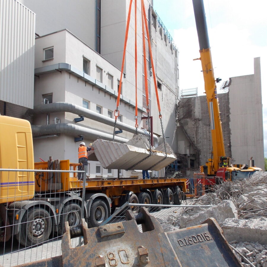 Bauarbeiten: Kranaushebung von Betonteilen auf einer Baustelle mit Abbrucharbeiten.