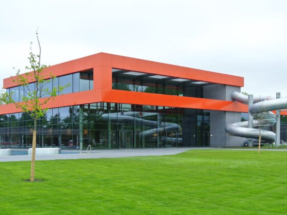 Moderne Architektur mit orangefarbenem Fassadenelement und Wasserrutsche in einer grünen Umgebung.