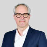 Geschäftsmann mit Brille in Anzug vor grauem Hintergrund. Professionelles Porträtfoto.