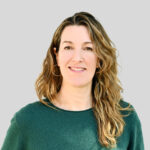 Portrait einer lächelnden Frau mit lockigem, braunem Haar und grünem Pullover.