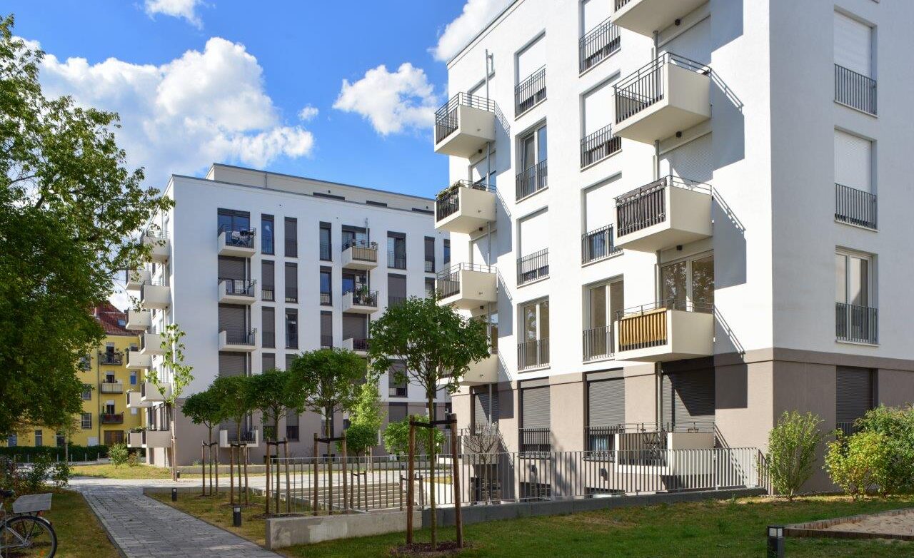 Moderne Wohnanlagen mit Balkonen und Grünflächen unter blauem Himmel.