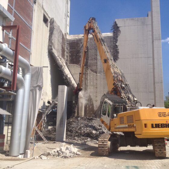 Bauarbeiten: Abrissmaschine entfernt Wand eines Gebäudes unter blauem Himmel.
