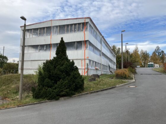 Sanierungsarbeiten an einem Gebäude, umhüllt mit Folie und orangefarbenen Markierungen.