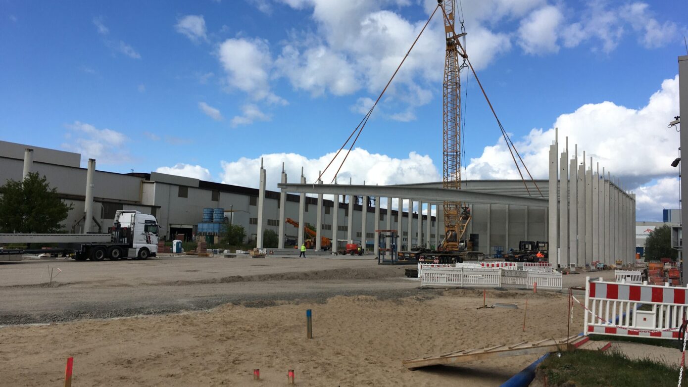 Bauplatz mit Kran und neuen Gebäudepfeilern unter blauem Himmel.