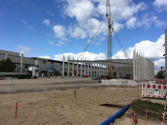 Bauplatz mit Kran und neuen Gebäudepfeilern unter blauem Himmel.