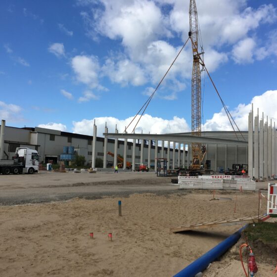 Bauplatz mit Kran und neuen Gebäudepfeilern unter blauem Himmel.