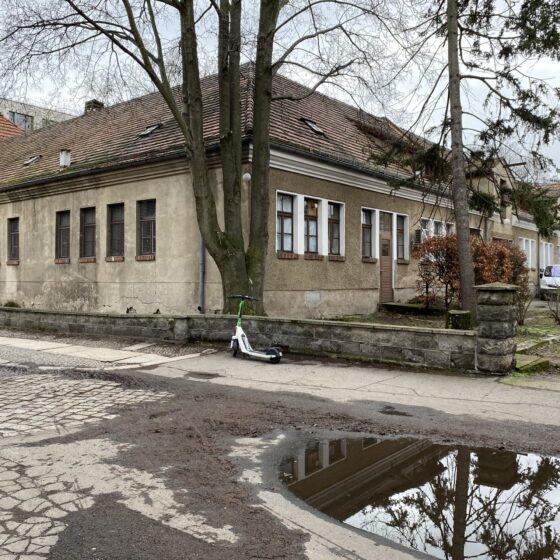 Verlassene Gebäude mit einem E-Scooter und Pfütze auf der Straße.