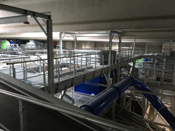 Moderne Industrieanlage mit Metallgerüsten und blauen Rohrleitungen in einem Innenraum.