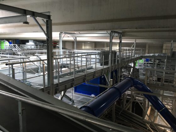 Moderne Industrieanlage mit Metallgerüsten und blauen Rohrleitungen in einem Innenraum.