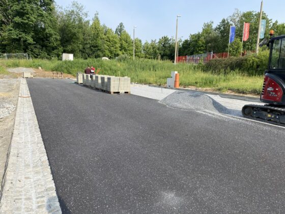 Bauarbeiten an einer neuen Straße mit Pflastersteinen und Maschinen im Hintergrund.