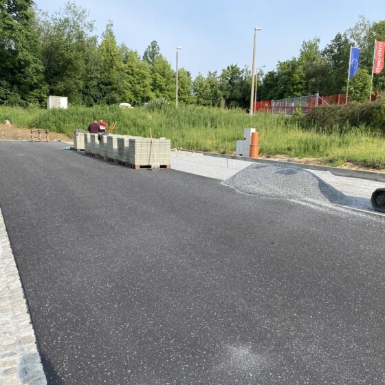 Bauarbeiten an einer neuen Straße mit Pflastersteinen und Maschinen im Hintergrund.