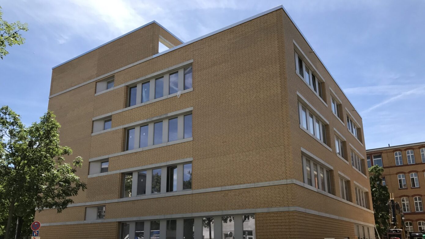 Neues modernes Gebäude mit Backsteinfassade und großen Fenstern in urbaner Umgebung.
