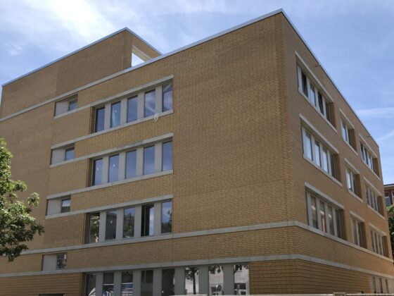 Neues modernes Gebäude mit Backsteinfassade und großen Fenstern in urbaner Umgebung.