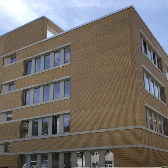 Neues modernes Gebäude mit Backsteinfassade und großen Fenstern in urbaner Umgebung.