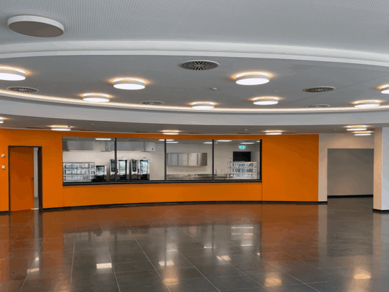 Moderne Innenansicht eines hellen Raumes mit orangefarbener Wand und großen Fenstern.