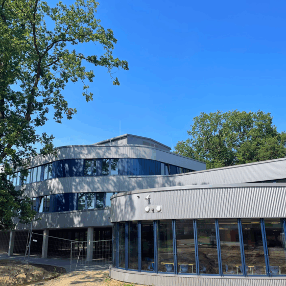 Johannes-Kepler-Gymnasium mit großen Fenstern und grünem Umfeld unter blauem Himmel.