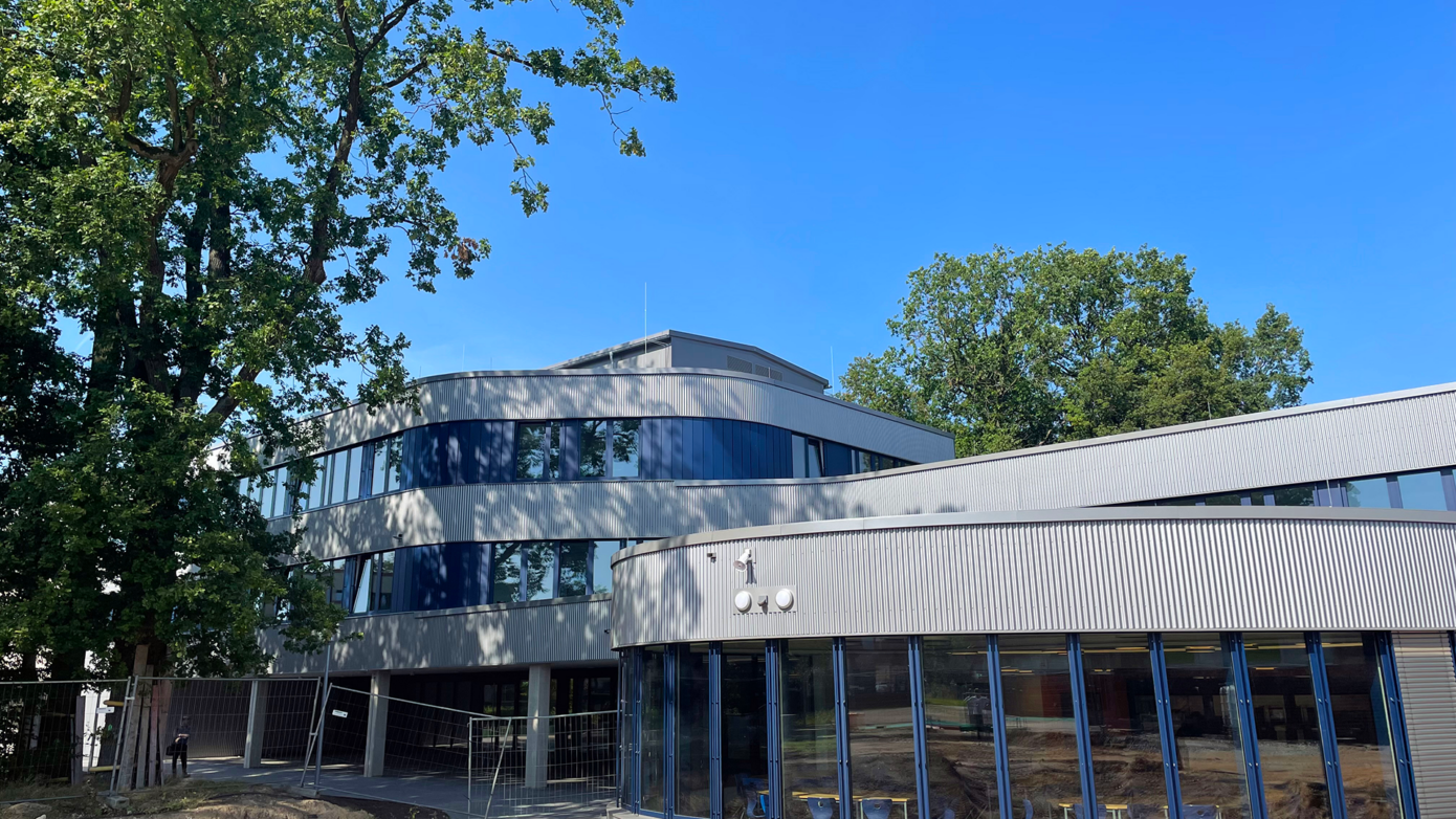 Johannes-Kepler-Gymnasium mit großen Fenstern und grünem Umfeld unter blauem Himmel.