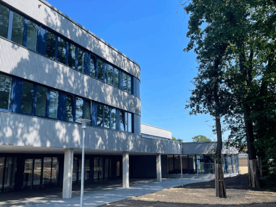 Moderne Architektur mit großen Fenstern und angrenzendem Freiraum unter blauem Himmel.