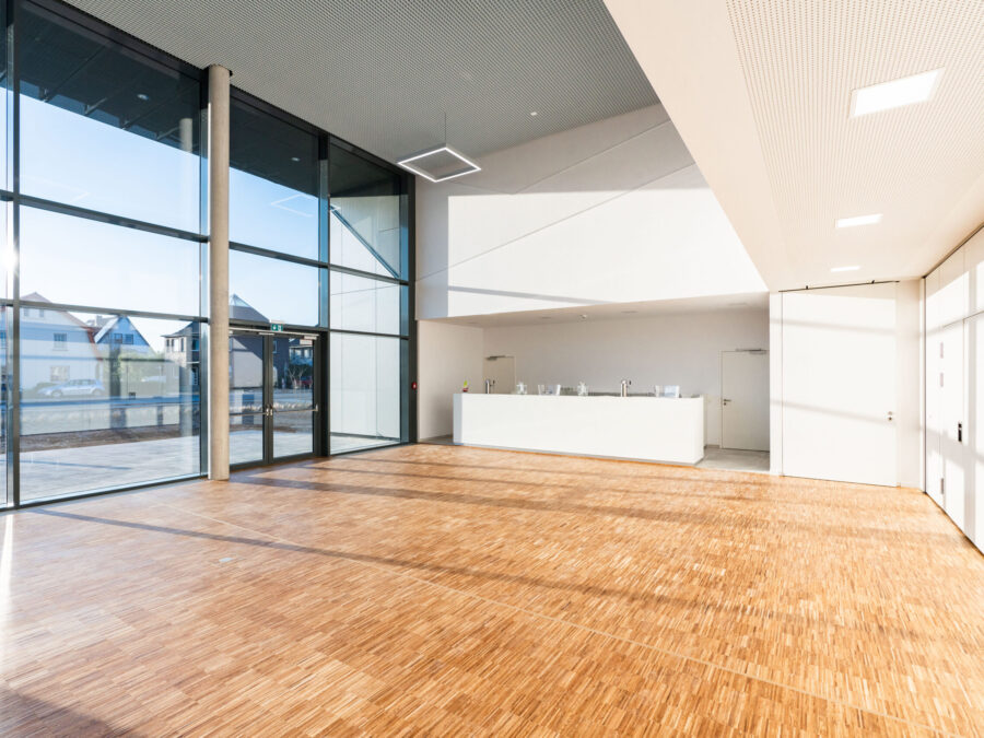 Heller, moderner Innenraum mit Holzfußboden und großen Fenstern. Empfangstresen im Hintergrund.