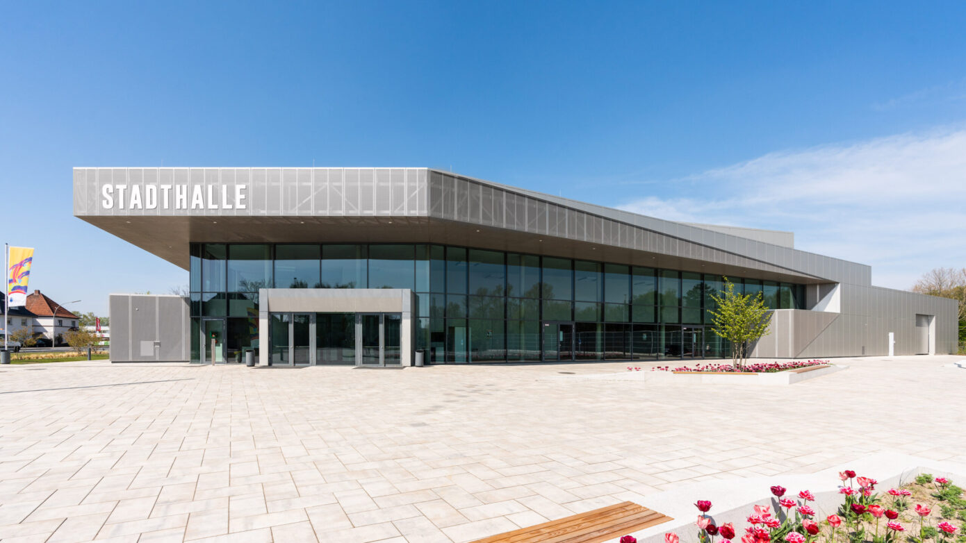 Stadthalle Rheda-Wiedenbrück mit Glasfassade und blühenden Blumen im Vordergrund.