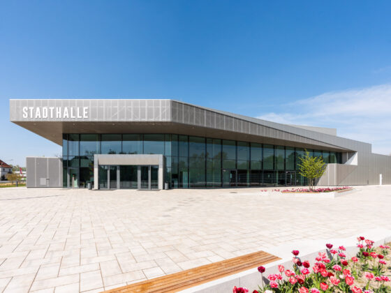 Stadthalle Rheda-Wiedenbrück mit Glasfassade und blühenden Blumen im Vordergrund.