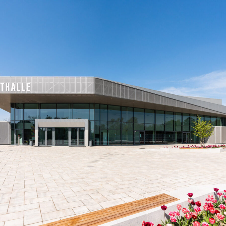 Stadthalle Rheda-Wiedenbrück mit Glasfassade und blühenden Blumen im Vordergrund.