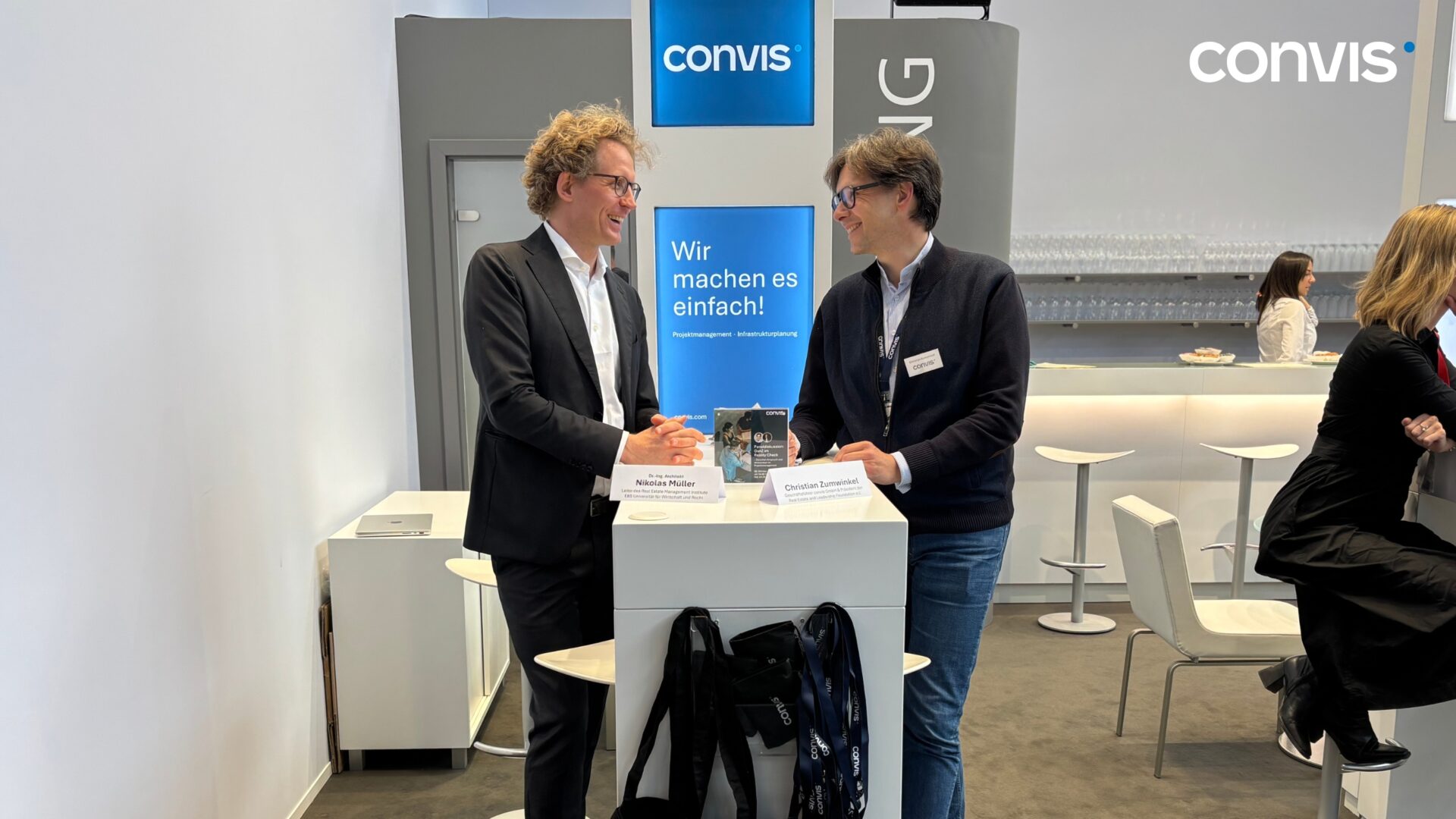 Zwei Personen im Gespräch an einem Messestand von Convis, mit informativen Materialien.