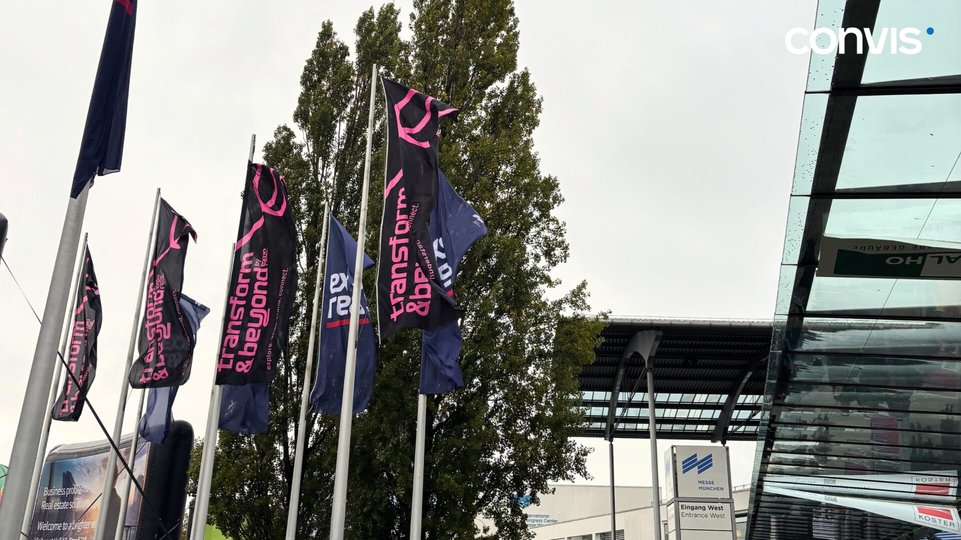 Fahnen mit dem Motto „transform & beyond“ vor einem modernen Gebäude.