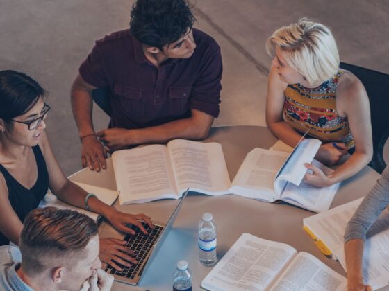 Studierende diskutieren gemeinsam über Bücher und Notizen an einem Tisch.