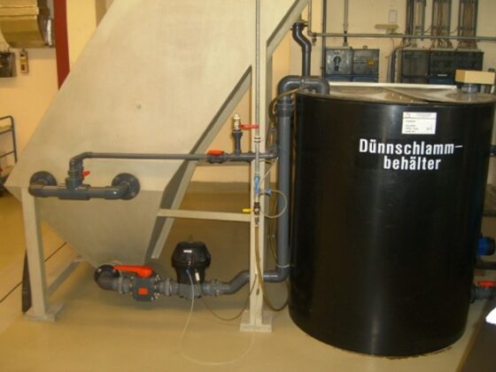 Dünnschlammbehälter mit Rohrleitungen und Pumpensystem in einer industriellen Umgebung.