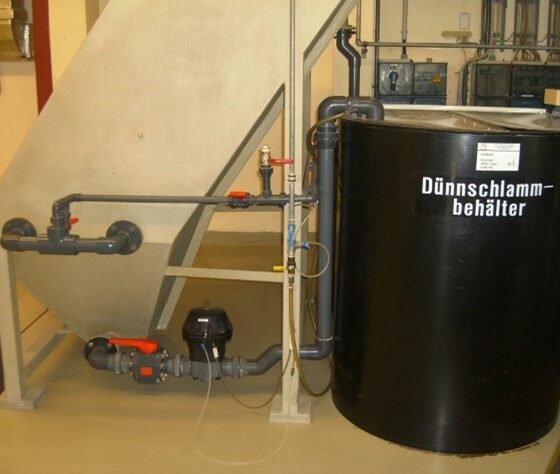 Dünnschlammbehälter mit Rohrleitungen und Pumpensystem in einer industriellen Umgebung.