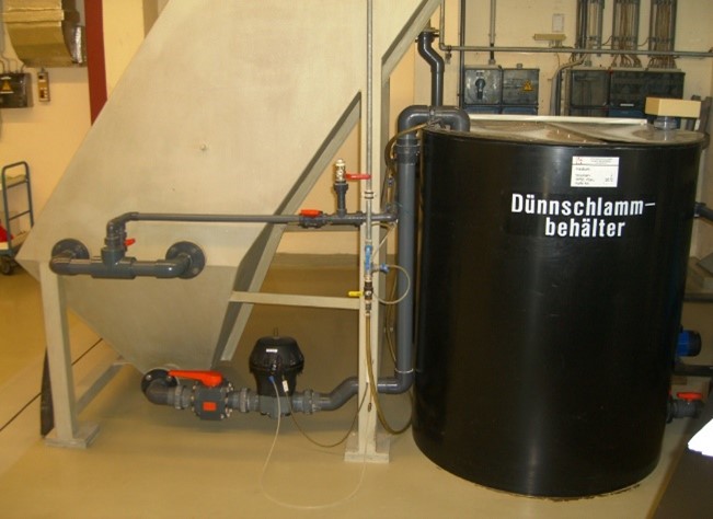 Dünnschlammbehälter mit Rohrleitungen und Pumpensystem in einer industriellen Umgebung.