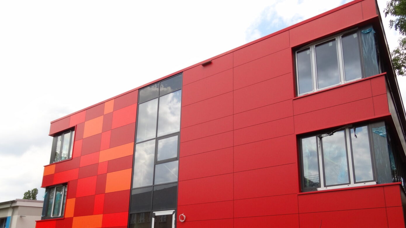 Rotes Gebäude mit bunten Fassadenelementen und Baustellenumgebung.