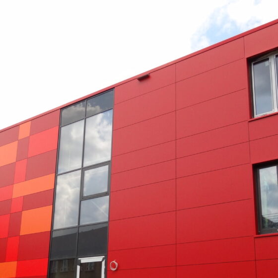 Rotes Gebäude mit bunten Fassadenelementen und Baustellenumgebung.