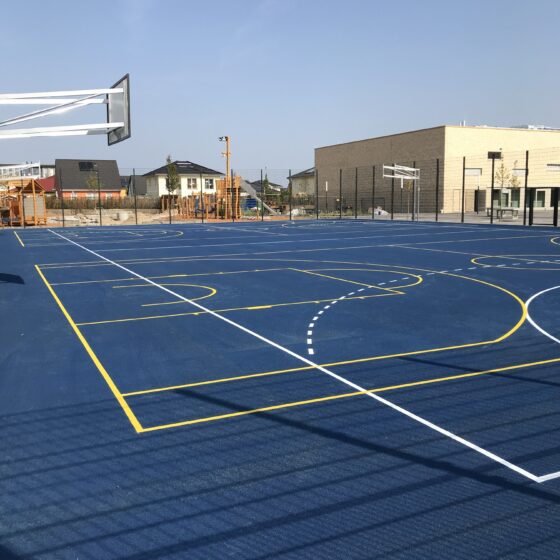 Neuer Sportplatz mit Basketballfeld und Spielgeräten unter klarem Himmel.