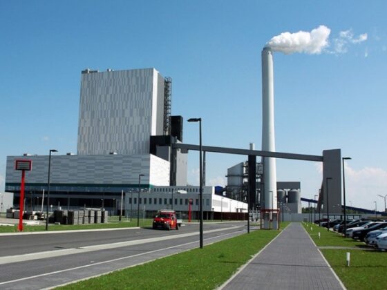 Moderne Industrieanlage mit Schornstein und Fahrzeugen auf dem Parkplatz.