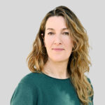 Porträt einer Frau mit lockigem Haar vor grauem Hintergrund.