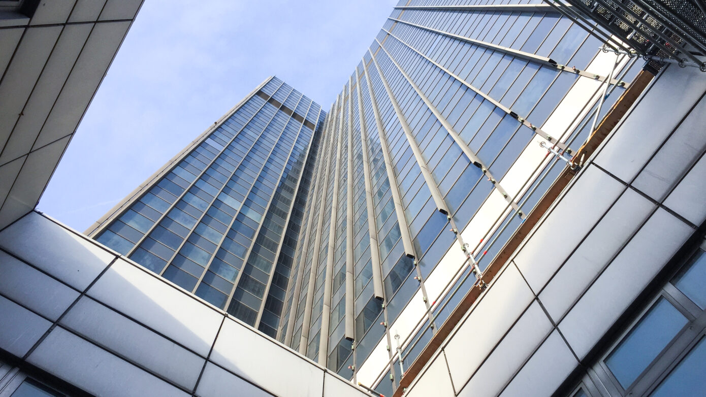 Blick nach oben auf moderne Wolkenkratzer mit Glasfassade und klar blauem Himmel.